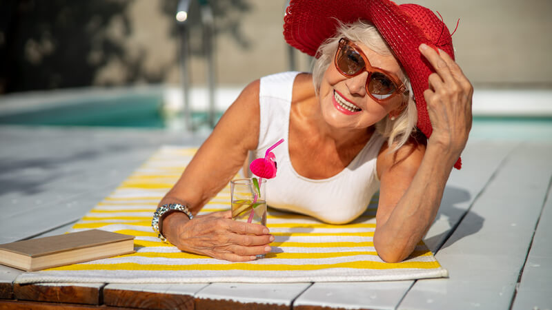 Smiling older woman in a red sun hat beside pool.