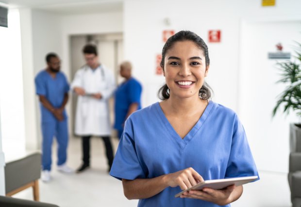 One focused person standing in front of a group of unfocused people smiling while wearing scrubs