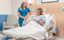 A maternity nurse standing next to a patient in her bed